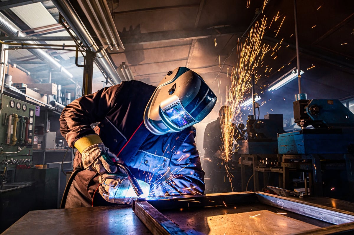 Welder joining metal parts with a torch, throwing sparks in a workshop