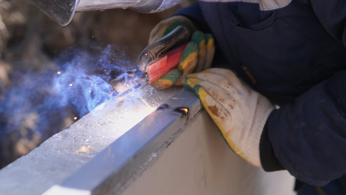 Welder finishing a seam with precise hand control, smoothing the weld bead on steel