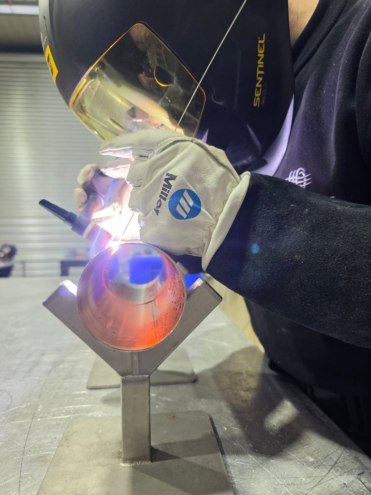 Welder in a Sentinel helmet TIG welding a stainless steel tube held in a V-block jig